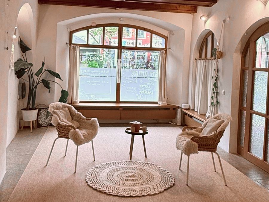 Der Praxisraum im Überblick: zwei Sessel mit Schaffellen und ein kleiner Tisch vor dem Bogenfenster, rechts die Eingangstür