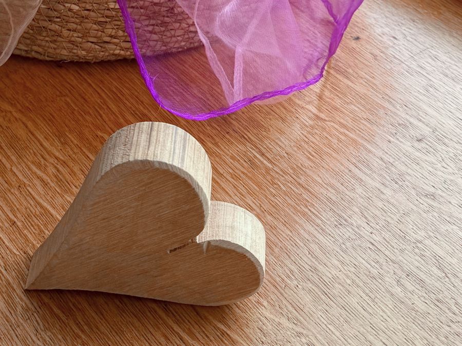 Ein Herz aus Holz auf dem Boden, dahinter ein Korb mit Tüchern